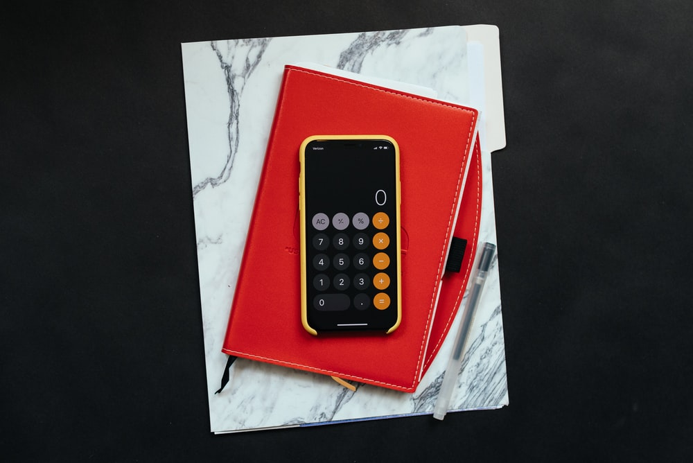 a calculator on a phone sitting on top of a red notebook.