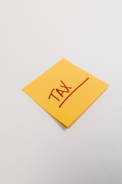  An image of an orange sticky note on white surface with “tax” written on it 